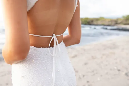 Back view of bride in elegant white dress with bow detail standing on Hawaii beach