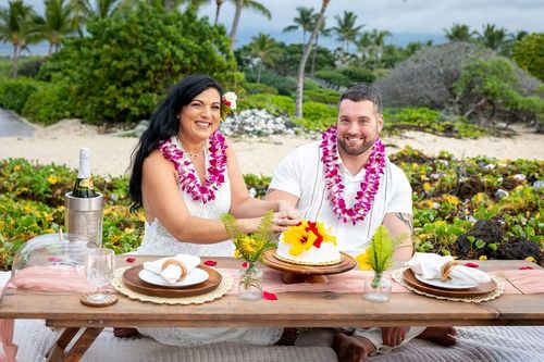 Couple celebrating with pink flower leis at outdoor dining experience with tropical palm trees in Hawaii