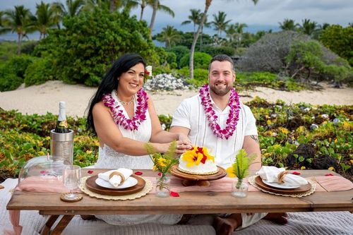 Wedding couple dining outdoors with traditional Hawaiian leis and tropical food spread