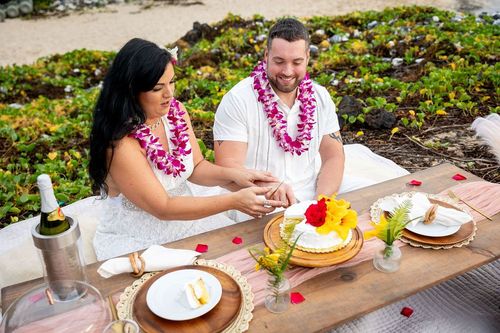 Couple with pink leis enjoying tropical cuisine at outdoor table with lush green mountains in Hawaii