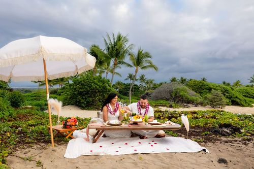 Luxury beach picnic setup with white umbrella, tropical flowers for Hawaii destination wedding