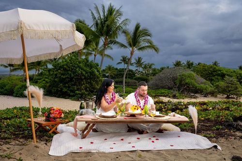 Romantic beach picnic under white umbrella with palm trees and dramatic scenery in Hawaii