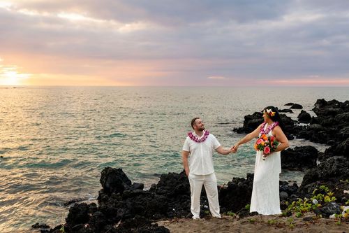 Couple holding hands silhouette on rocky beach during golden hour sunset in Hawaii