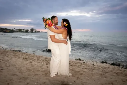 Bride placing traditional lei on groom during Hawaii beach wedding ceremony at sunset