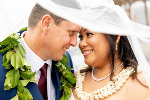 Groom wearing white orchid lei gazing at bride during Hawaii wedding ceremony