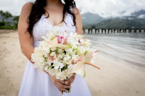 Bride holding pink and white tropical bouquet on historic wooden pier in Hawaii