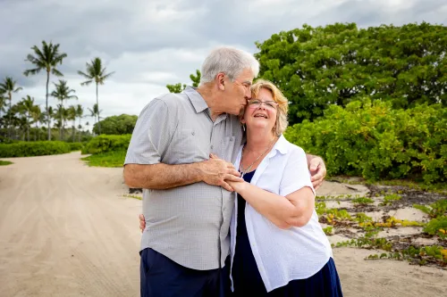 Couple embracing on beach with palm trees for Hawaii anniversary celebration