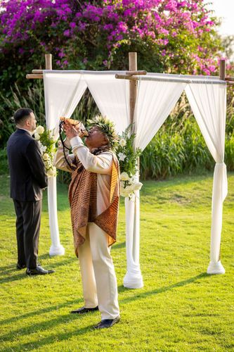 Wedding couple walking through floral archway on lush green golf course in Hawaii
