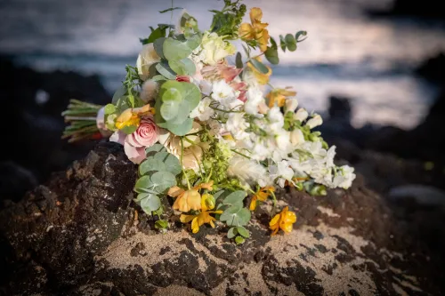 Tropical wedding bouquet with white orchids and yellow flowers on lava rock in Hawaii