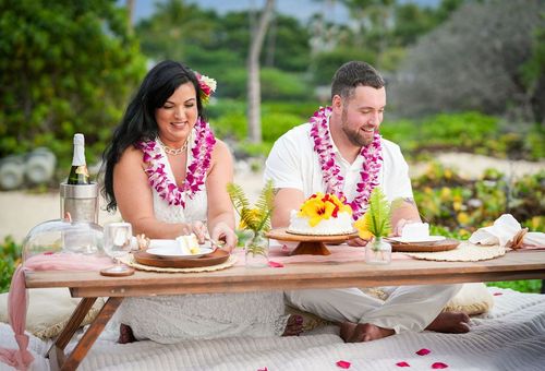 Couple sharing intimate meal at outdoor table with pink flower leis in Hawaii