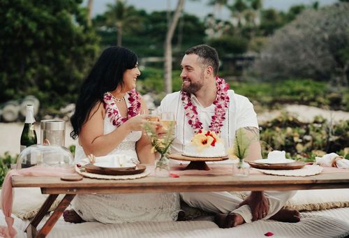Couple enjoying outdoor dining experience with traditional Hawaiian leis and tropical cuisine