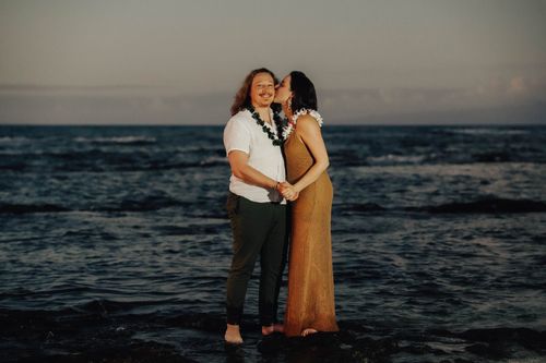 Couple embracing on Hawaii beach at twilight with ocean waves and cloudy sky