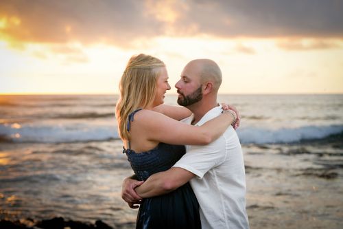 Couple standing in ocean waves embracing at golden hour sunset in Hawaii