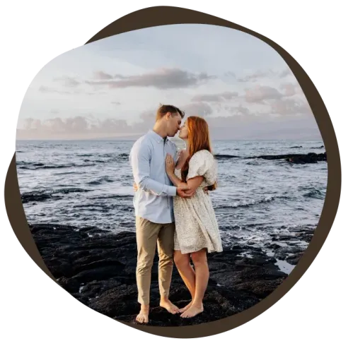 Newlywed couple embracing on dark lava rocks at twilight beach in Hawaii